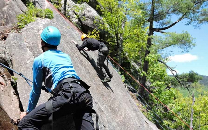 two people wearing rock climbing gear climb a rock face in maine on an outward bound trip